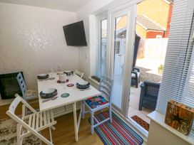 A dining area with a white table set for four with chairs and a wall mounted television next to glass doors leading to a patio at Ty Bach Twt Llanelli