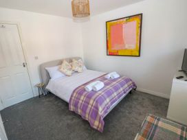 A bedroom with a double bed with purple plaid blanket towels and floral pillows a colorful abstract painting on the wall at Ty Bach Twt Llanelli
