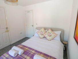 A bedroom with a bed with floral pillows and rolled towels on a purple plaid blanket at Ty Bach Twt Llanelli