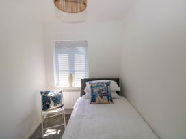 A small bedroom with a single bed a chair with a cushion and a window with blinds at Ty Bach Twt Llanelli in Llanelli