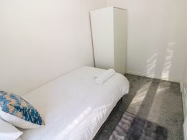 A small bedroom with a single bed white bedding a patterned pillow a rolled towel a white wardrobe and grey carpet at Ty Bach Twt Llanelli