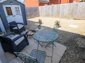 A backyard with a small table and chairs a fire pit wood logs and a shed with a wooden fence at Ty Bach Twt Llanelli