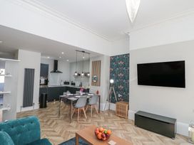 An open plan kitchen and dining area with black cabinets dining table with chairs wall mounted tv and a tripod lamp at Porto Brid in Bridlington