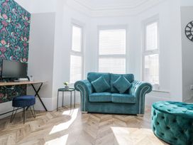 A living room with a teal sofa and matching ottoman near bay windows with blinds at Porto Brid in Bridlington