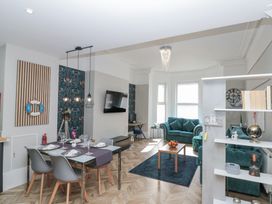 An open living and dining area with a dining table, chairs, two teal sofas, coffee table, wall mounted TV, and shelves at Porto Brid in Bridlington