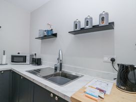 A kitchen counter with a sink a microwave a toaster a kettle and shelves holding containers and a flower pot at Porto Brid in Bridlington