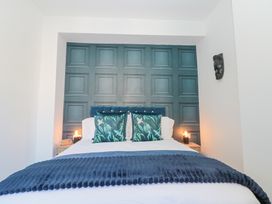 A bed with blue and green pillows and a blue blanket in a bedroom with paneled wall and two bedside tables with lamps at Porto Brid in Bridlington