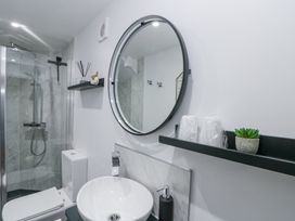 A bathroom with a round mirror a white sink a toilet a glass shower and shelves with toiletries at Porto Brid in Bridlington