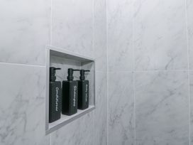 Three black pump bottles labeled conditioner shampoo and body wash on a built-in shelf in a shower with white marble tiles at Porto Brid in Bridlington