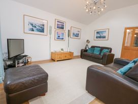 A living room with two brown leather sofas a brown leather ottoman a wooden coffee table a television on a black stand and framed pictures on the wall at Pippin Cottage in Beaumaris