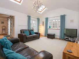 A living room with leather sofas teal cushions a wooden table a television and light blue curtains at Pippin Cottage in Beaumaris