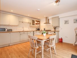 A kitchen with wooden floor cabinets a dining table with four chairs and a plant at Pippin Cottage in Beaumaris