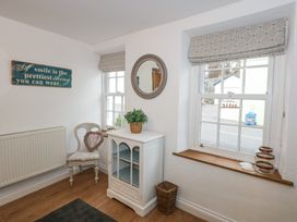 A corner of a room with a white cabinet topped with a green plant a chair with a heart-shaped wreath and two windows with Roman blinds at Pippin Cottage in Beaumaris