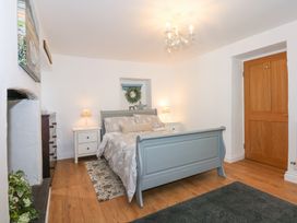 A bedroom with a blue bed frame bedside tables with lamps a wooden door and wooden floor at Pippin Cottage in Beaumaris