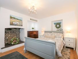 A bedroom with a gray bed frame two bedside tables lamps and a wooden chest of drawers at Pippin Cottage in Beaumaris