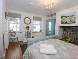 A bedroom with a bed folded towels a blue wardrobe a chair cabinet and two windows at Pippin Cottage in Beaumaris