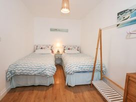 A bedroom with two single beds a nightstand with a lamp and a wooden clothes rack at Pippin Cottage in Beaumaris