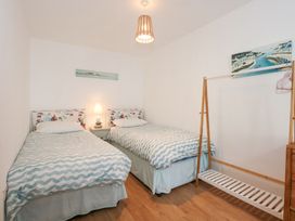 A bedroom with two single beds a bedside table with a lamp a wooden clothes rack and paintings on the walls at Pippin Cottage in Beaumaris