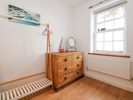 A room with a wooden dresser a standing mirror two model boats a wooden clothing rack with pink hangers and a window with a radiator below at Pippin Cottage in Beaumaris