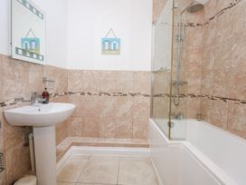 A bathroom with a pedestal sink a mirror a bathtub with a shower and tiled walls at Pippin Cottage in Beaumaris