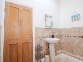 A bathroom with a wooden door a pedestal sink a mirror and beige tiled walls at Pippin Cottage in Beaumaris