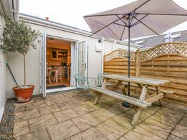 An outdoor patio with a wooden picnic table and umbrella two metal chairs a potted tree and French doors leading to a kitchen at Pippin Cottage in Beaumaris