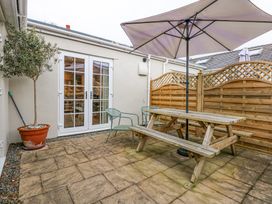 An outdoor patio area with a wooden picnic table and umbrella two metal chairs a potted tree and wooden fencing at Pippin Cottage in Beaumaris