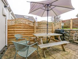 A patio with a wooden picnic table and umbrella two metal chairs wooden fence and a barbecue grill at Pippin Cottage in Beaumaris