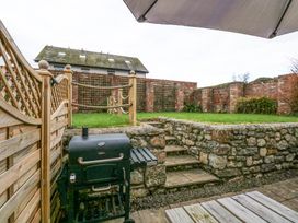 An outdoor patio area with a black barbecue grill stone steps leading to a raised lawn with wooden posts and rope fencing and a brick wall in the background at Pippin Cottage in Beaumaris
