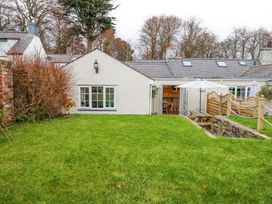 A garden with green grass and shrubs outside a white house with windows and a patio door at Pippin Cottage in Beaumaris