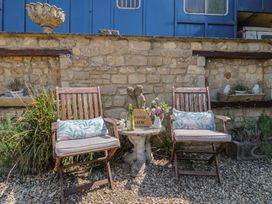 Two wooden chairs with cushions and a small stone table with flowers and a wine bottle against a stone wall at Pond View at Yeabridge Farm in Whetley Cross near Mosterton