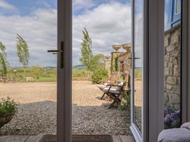 View through an open glass door to a gravel patio with wooden chairs and stone planters with a grassy area and trees beyond at Pond View at Yeabridge Farm in Whetley Cross near Mosterton