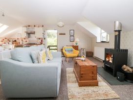 A living room with a sofa yellow armchair wood stove and kitchen area at The Hayloft in Lostwithiel