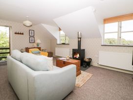 A living room with a light blue sofa a yellow armchair a wood burning stove and windows at The Hayloft in Lostwithiel
