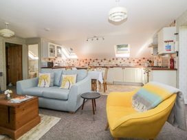 An open plan living area with a light blue sofa, yellow armchair, wooden chest, dining table, and kitchen with white cabinets at The Hayloft in Lostwithiel