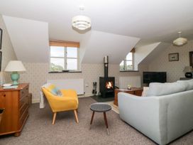 A living room with a yellow armchair a gray sofa a wood stove and a wooden dresser at The Hayloft in Lostwithiel