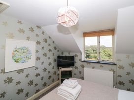 A bedroom with a bed folded towels a small television on a stand a window and patterned wallpaper at The Hayloft in Lostwithiel