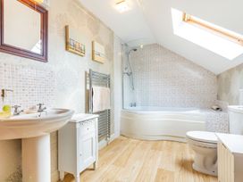 A bathroom with a bathtub shower combination under a skylight a toilet a pedestal sink a mirror and wooden flooring at The Hayloft in Lostwithiel