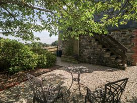 A small outdoor seating area with metal chairs and a table under a tree near stone steps at The Hayloft in Lostwithiel