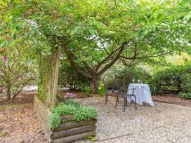 An outdoor seating area with a small round table covered with a white cloth and two metal chairs under a tree at The Hayloft in Lostwithiel