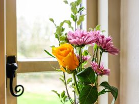 A close up of a yellow rose and pink flowers in a vase in front of a window at The Mill in Lostwithiel