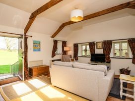 A living room with a sofa a television wooden beams and an open door showing green grass at The Mill in Lostwithiel