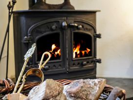 A burning wood stove with fire tools and logs in a basket at The Mill in Lostwithiel