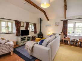 A living room with a gray sofa a wood stove a dining table and patterned curtains at The Mill in Lostwithiel