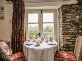 A small table set for tea with cups plates scones flowers near a window with curtains and stone wall at The Mill in Lostwithiel
