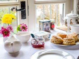A table set with scones jam clotted cream teapot cup and flowers by a window at The Mill in Lostwithiel