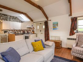 A living room with a gray sofa and kitchen with white cabinets and stone wall at The Mill in Lostwithiel