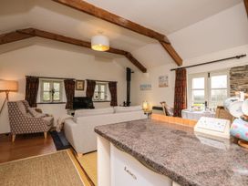 An open living room and kitchen area with sofas armchair small dining table and wooden ceiling beams at The Mill in Lostwithiel