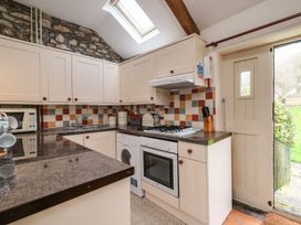 A kitchen with white cabinets a stone wall and a door opening to a garden at The Mill in Lostwithiel