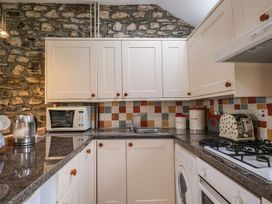 A kitchen with white cabinets brown knobs a stone wall microwave kettle sink washing machine toaster and stove at The Mill in Lostwithiel